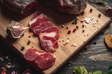 Sliced jerky. Sausage stick sliced on the board. Garlic red peppers and green parsley near the cold...
