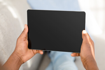 Naklejka premium Unrecognizable black man using digital tablet with black blank screen, mockup for application or website advertisement