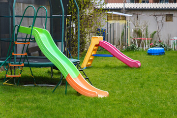 Plastic multi-colored slides on the playground. Green grass on the lawn.