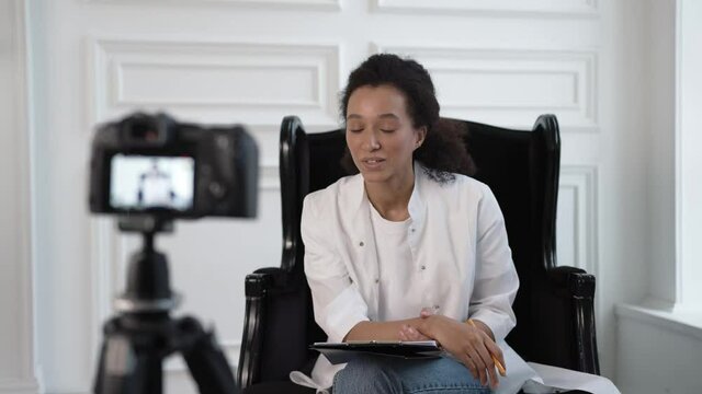 Beautiful african woman in white lab coat with pencil in hand, in front of the camera speaking and explaining. Lecturer, online video class and courses on medical treatment and research