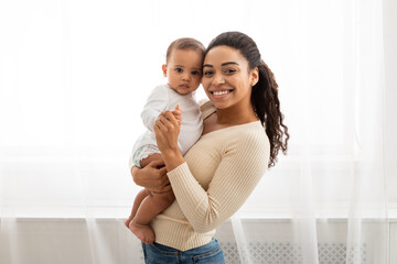 Black Mom Holding Little Infant Smiling To Camera Posing Indoors