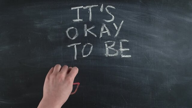 Words it is okay to be gay are written by hand on a chalkboard, timelapse. Concept of tolerance and understanding sexual minorities.