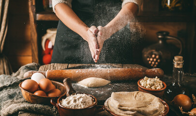 Woman hands cooking dough on rustic wooden background. White flour flying into air. Cooking bread...