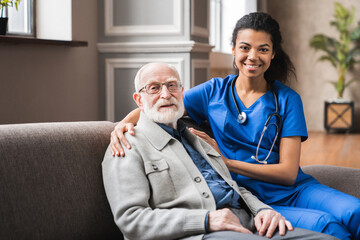 Front view portrait of caring afro nurse taking care of an elderly caucasian man grandfather...