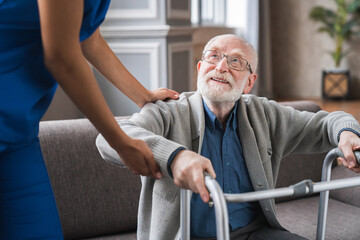 Close up shot of a young nurse helping disabled senior man with standing using walker. Cropped shot...