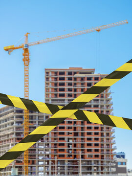 barrier prohibition tape on blurred background of building under construction with high-rise crane, ban on construction, low-quality residential buildings, construction crisis