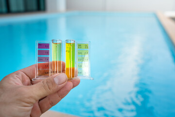 Checking water quality of swimming pool by using chemical test kit to compare PH and chlorine concentration, photo with blurred background of clearly blue water surface.