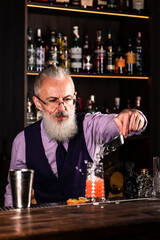 Stylish brutal barman makes a cocktail at bar counter background