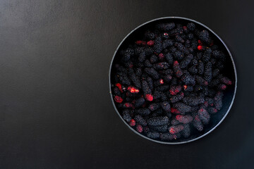 Ripe black mulberries on a black iron plate. Placed on a black cement floor.