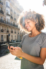smiling young black woman looking at cellphone in city