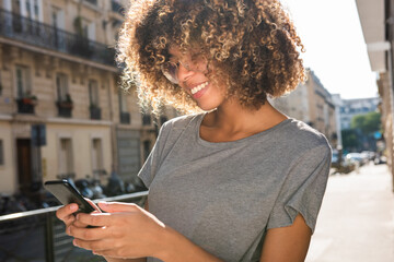 Fototapeta na wymiar smiling black girl looking at mobile phone in city