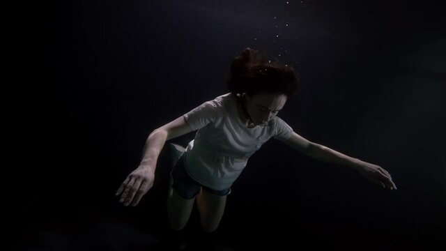 adult woman is sinking in depth of sea or river, closed eyes, breathless body, subaquatic shot