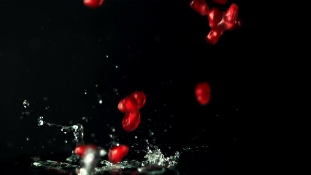 Super slow motion pomegranate grains fall into the water with splashes. On a black background. Filmed on a high-speed camera at 1000 fps.High quality FullHD footage