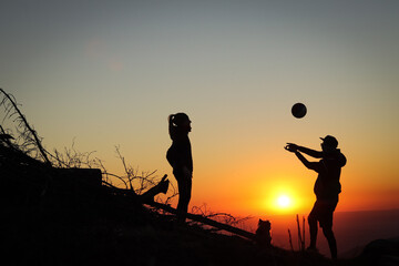 Two young athletes man and woman aged 25-30 playing volleyball on top of the mountain at sunset. Sports moment. Active life. Overhead passing. Volleyball bump, stroke, hitting