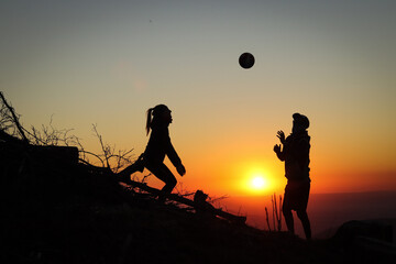 Two young athletes man and woman aged 25-30 playing volleyball on top of the mountain at sunset. Sports moment. Active life. Overhead passing. Volleyball bump, stroke, hitting