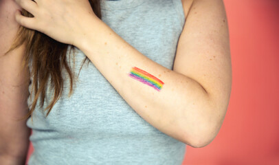 Fototapeta na wymiar Portrait of a young woman with rainbow Flag on cheek and body, the LGBT community on a colorful pink background