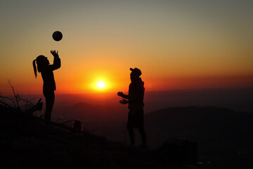 Fototapeta na wymiar Young volleyball couple enjoying the top of a pink mountain with a ball at sunset. Silhouettes of a woman and a player pinching their fingers with a ball. Volleyball spiking, bump. Overhead passing