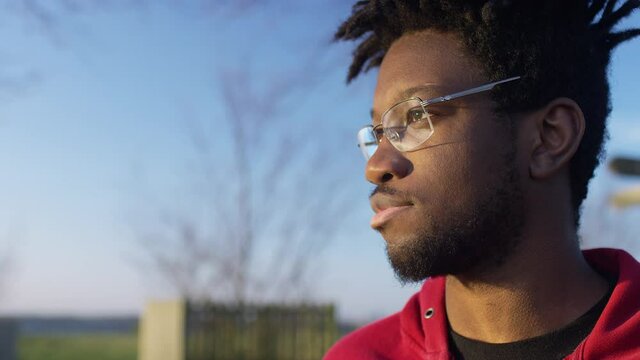 Close side profile shot of young black male with cool hair staring off towards the sunset, in slow motion