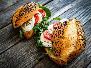 Caprese sandwich with tomato, mozzarella and arugula on wooden table
