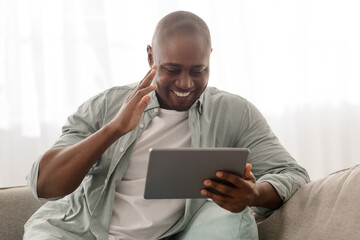 Cheerful african american mature man having video call, using digital tablet, smiling and waving hand to screen