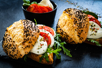 Caprese sandwich with tomato, mozzarella and arugula on wooden table
