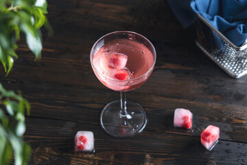 Elegant glass of pink rose champagne with frozen raspberries in ice cube