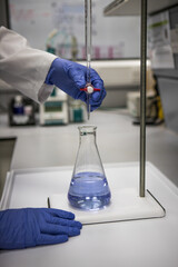 Chemist with gloved hands in a laboratory analysing a sample by titration 