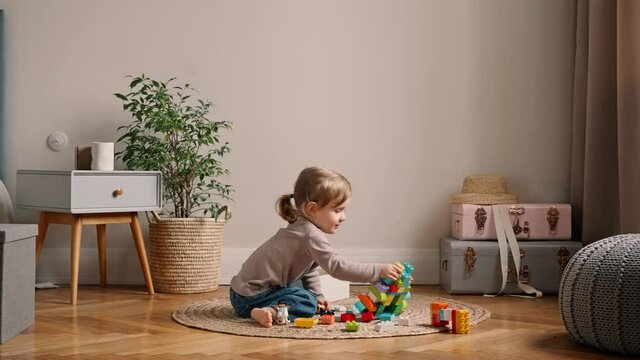 4k little girl sitting on the floor and playing with colorful blocks building blocks. Pretty child having fun playing with plastic constructor. Assembling plastic toy bricks, education toy. slow motion
