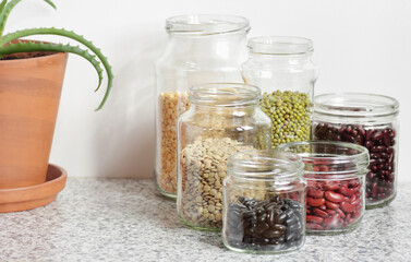 Variety of dry legumes: kidney bean, peas, green gram in glass jars uncooked on white kitchen background, zero waste, eco friendly, balanced diet food, healthy clean eating, vegan protein concept
