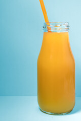Fresh orange juice bottle glass against blue background. Summer freshness concept.