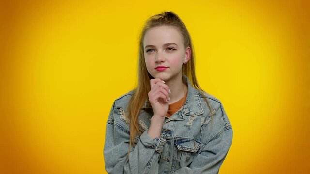 Thoughtful clever teenager student girl 20s years old rubbing her chin and looking aside with pensive expression, pondering a solution, doubting question. Young adult woman on yellow wall background