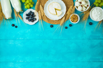 Jewish holiday Shavuot background with cheese, milk bottle, wheat ears and fruits on wooden blue table
