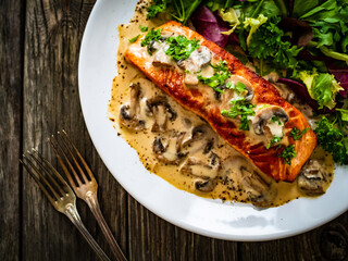 Fried salmon steak in mushroom sauce and vegetable salad served on wooden table
