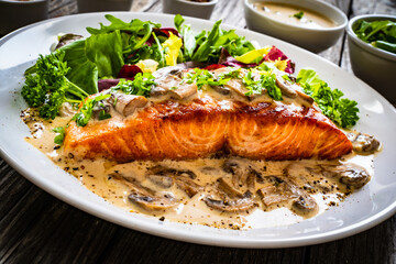Fried salmon steak in mushroom sauce and vegetable salad served on wooden table
