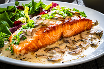 Fried salmon steak in mushroom sauce and vegetable salad served on wooden table

