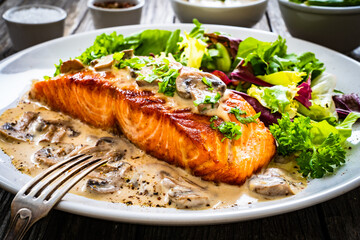 Fried salmon steak in mushroom sauce and vegetable salad served on wooden table
