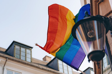 Lgbt rainbow flag located on the facade of a building with a old fashioned lamp on it.