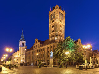 Fototapeta na wymiar Torun, Poland. Old Town Market Square at dawn with Nicolaus Copernicus Monument in front of the Old Town Hall, and Church of the Holy Spirit in the background. The monument was erected in 1853.