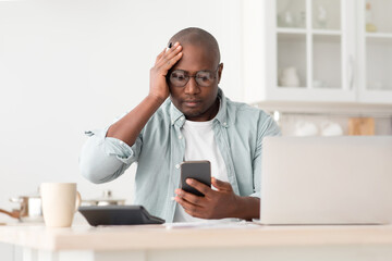 Expensive modern life. Worried black mature man calculating utility charges and bills, using...