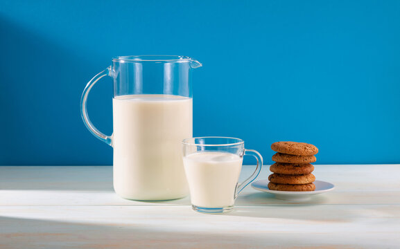 A jug and a glass of milk with cookies on a wooden table, on a blue background.Copy space.