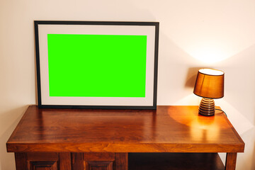 Empty painting in a black frame stands on a wooden table near a glowing night light