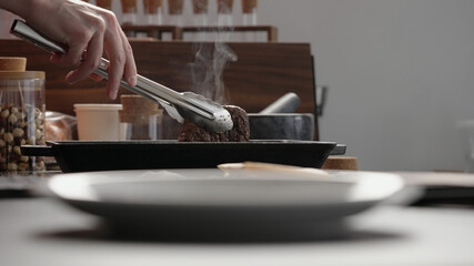man hand use tongs to pick up beef steak from grill pan