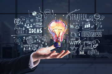 Businessman hand holding hologram of colorful light bulb as a concept of new idea for start up. Concept of creativity and brainstorming. Panoramic office open space on background