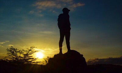 silhouette of a person standing on a rock in the sunset