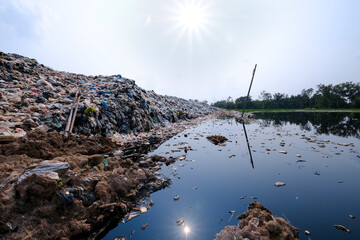 Polluted water and mountain large garbage pile and pollution at the sun the background, Pile of...
