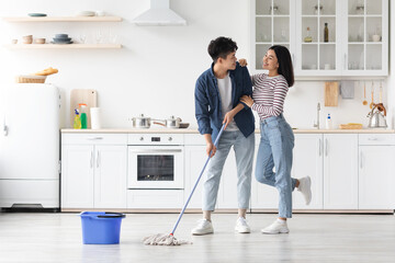 Loving asian couple mopping floor in kitchen