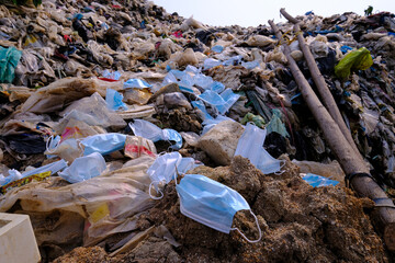 Discarded used medical face masks along and garbage trash with other plastic debris lies on the ground