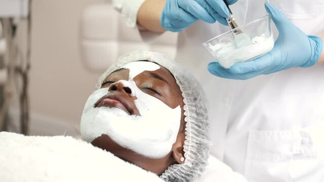 Cosmetologist applies alginate mask with spatula on face of woman