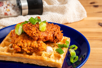 Homemade Southern American comfort street food fresh deep fried crispy stacked chicken wings with buffalo red chili spicy hot sauce and waffle sweet maple syrup