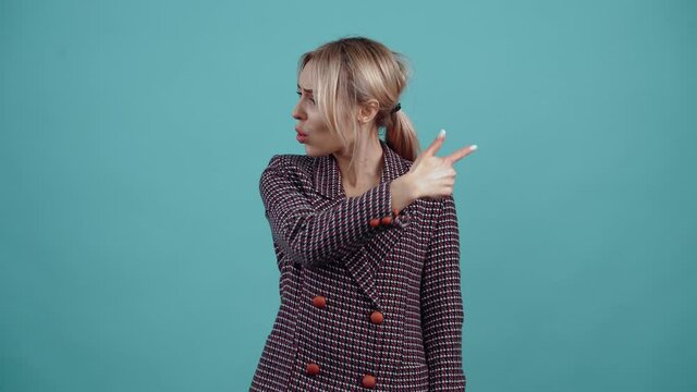 The charismatic young woman suddenly turns her head and index finger in opposite directions, shows her friend something shocking, looks subtle.Isolated on a turquoise background. The concept of life